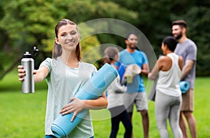 Smiling woman with yoga mat and bottle at park