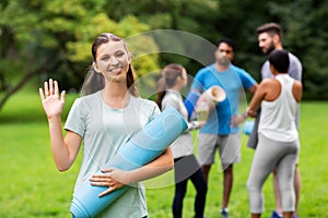 Smiling woman with yoga mat waving hand at park
