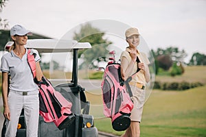 smiling women in polos and caps with golf equipment at golf course photo