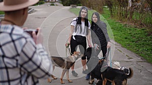 Smiling women posing with group of dogs as man taking photo. Caucasian pet walkers enjoying overcast morning with