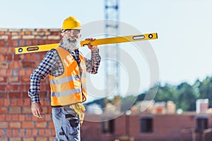 Smiling worker in reflective vest and hardhat walking with spirit level across