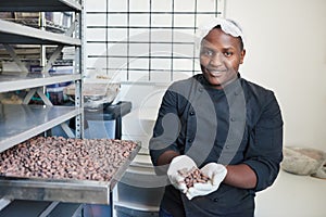 Smiling worker selecting cocoa beans from a factory tray