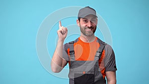 Smiling workerman in uniform raised finger up as sign he has new idea on blue background