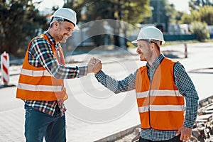 Smiling workers in reflective vests and white helmets greeting e