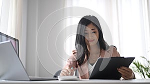 Smiling working woman holding clipboard and using calculator.