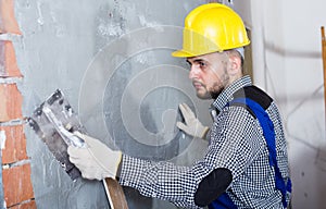 Smiling workman in the helmet is plastering the wall