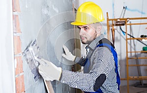 Smiling workman in the helmet is plastering the wall