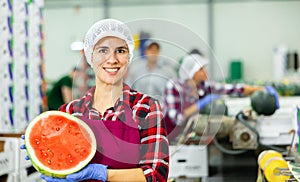 Smiling workwoman of fruit sorting factory standing with half of watermelon