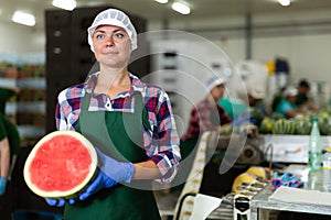 Smiling workwoman of fruit sorting factory standing with half of watermelon