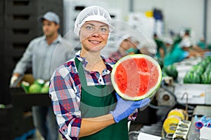 Smiling workwoman of fruit sorting factory standing with half of watermelon