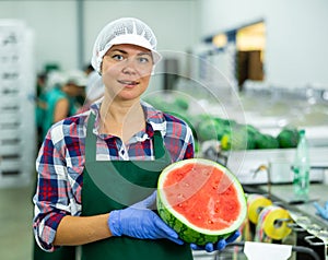 Smiling workwoman of fruit sorting factory standing with half of watermelon
