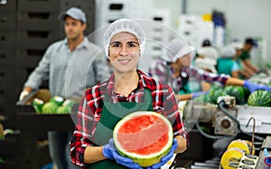 Smiling workwoman of fruit sorting factory standing with half of watermelon