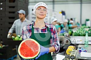 Smiling workwoman of fruit sorting factory standing with half of watermelon