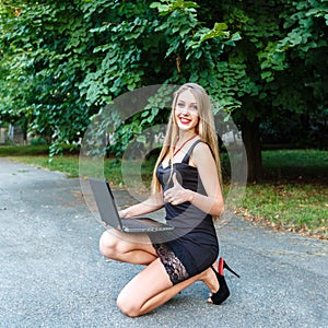 Smiling youg girl in black dress with laptop showing finger up.