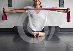 Smiling Young Active Female using a theraband exercise band to strengthen her arms muscles in the studio