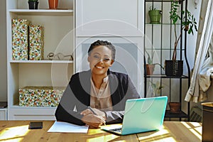 Smiling Young adult entrepreneur freelance black woman small business owner with laptop and smartphone working in home