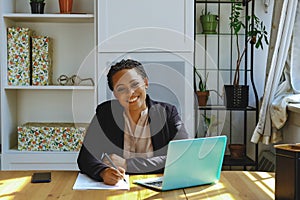 Smiling Young adult entrepreneur freelance black woman small business owner with laptop working in home office looking