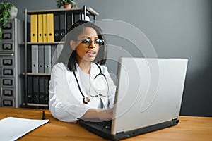 Smiling young adult indian female doctor wear white coat in medical clinic office. Happy beautiful health care india