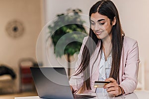 Smiling young adult woman, checking prices online, holding credit card