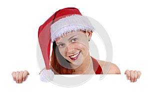 Smiling young adult woman in Christmas Santa hat holding plain white blank advertising board, copy space