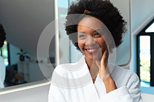 Smiling young african american afro woman looking away while wearing bathrobe in bathroom