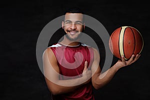 Smiling young African-American basketball player in sportswear isolated over dark background.