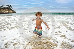 Smiling young African American boy running and playing at the beach while on a family vacation