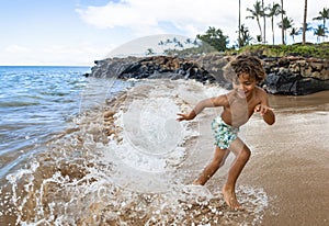 Smiling young African American boy running and playing at the beach while on a family vacation