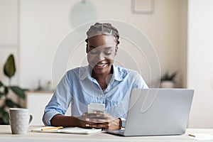 Smiling young african american businesswoman using smartphone at workplace in office