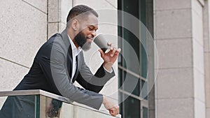 Smiling young african american corporation employee, manager, businessman drinking coffee on balcony during break