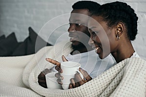 smiling young african american couple holding cups and looking away
