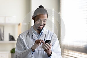 Smiling young African American doctor using cellphone.