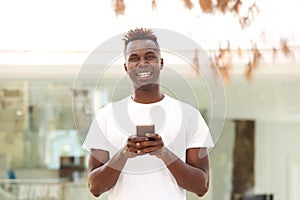 Smiling young african american man with mobile phone standing outside in city