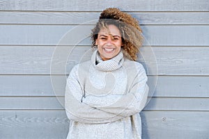 Smiling young african american woman with curly hair and arms crossed against gray wall