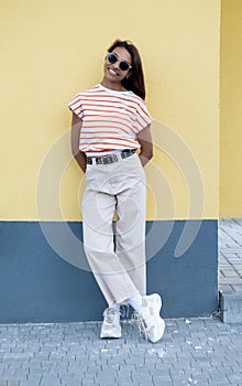 Smiling young african american woman girl in casual t-shirt, eyeglasses posing isolated on yellow orange wall background studio.