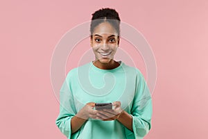 Smiling young african american woman girl in green sweatshirt posing isolated on pastel pink background in studio