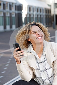 Smiling young african american woman holding mobile phone outside