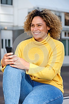 Smiling young african american woman with mobile phone in city