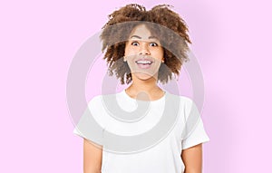 Smiling young african american woman with perfect skin care and healthy curly afro hair isolated on pink background. Blank t shirt