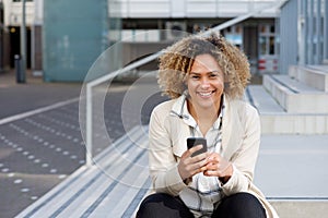 Smiling young african american woman with phone outside