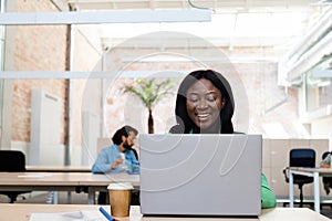 Smiling young african american woman working in the office using laptop. Copy space.
