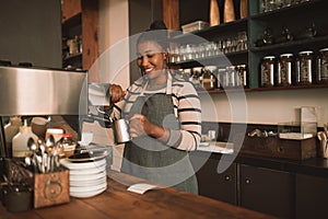 Smiling young African barista frothing milk behind a cafe counter