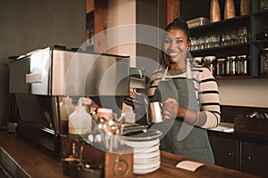 Smiling young African barista preparing coffee behind a cafe counter