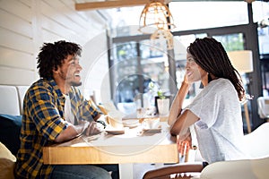 Smiling young african couple sitting at a table at a cafe drinking coffee and talking together