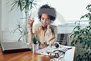 Young African female entrepreneur sitting at a desk in her home office using digital tablet and drink wine