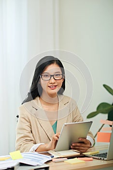 Smiling young African female entrepreneur working online with a digital tablet while sitting at a table in her home office