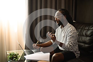 Smiling young African man freelancer having video call on laptop during working at home