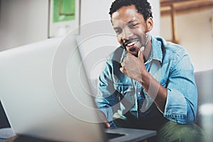 Smiling young African man making video call with friends while sitting on sofa at his modern office.Concept of happy