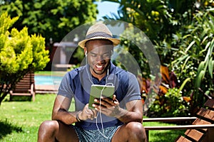 Smiling young african man sitting outdoors using digital tablet