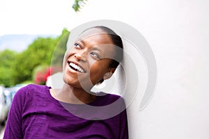 Smiling young african woman leaning against wall